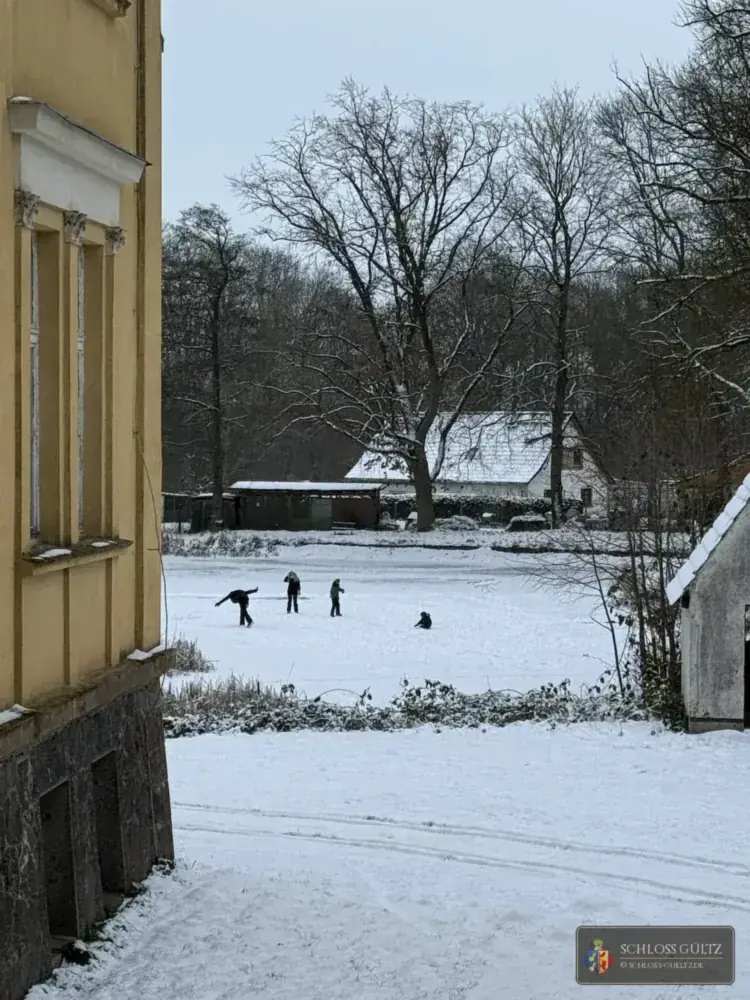 Winterblick aus dem Schloss auf Schlittschuhläufer auf dem zugefrorenen Schlossteich