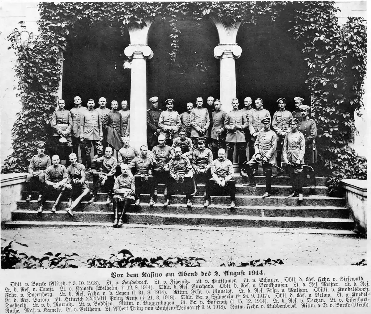 Gruppenbild von rund vierzig Offizieren in Felduniform auf der Freitreppe vor dem efeuberankten Säulenportal des Offizierskasinos in Pasewalk, darunter die Namensliste