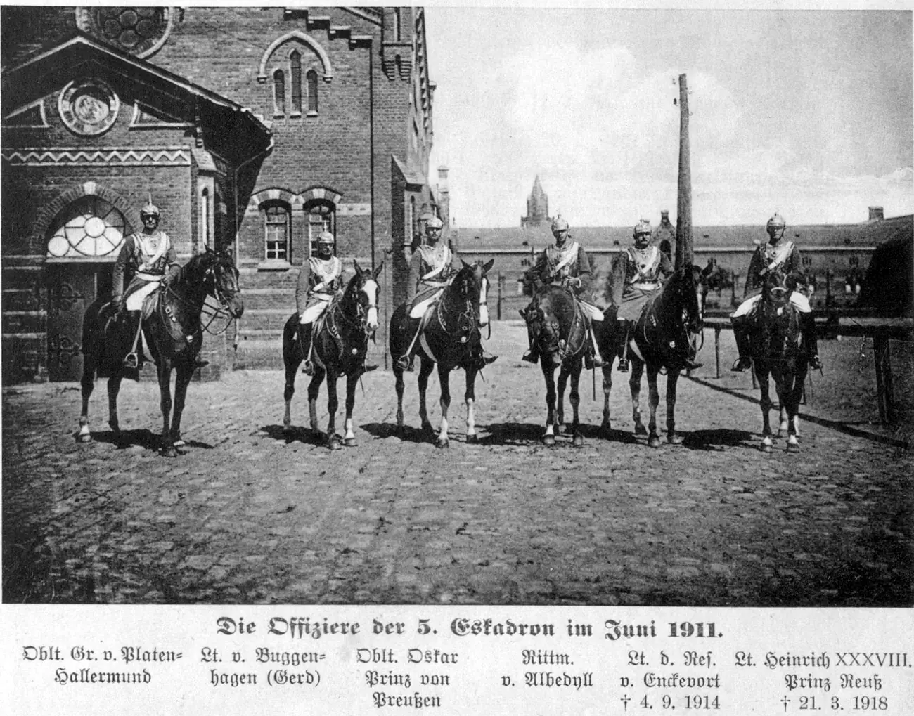 Sechs berittene Offiziere mit Helm und Kürass nebeneinander auf dem Kasernenhof, links ein Backsteinbau mit Rundfenster; darunter die Namen: Oblt. Gr. v. Platen-Hallermund, Lt. v. Buggenhagen (Gerd), Oblt. Oskar Prinz von Preußen, Rittm. v. Albedyll, Lt. d. Res. v. Enckevort, Lt. Heinrich XXXVIII. Prinz Reuß