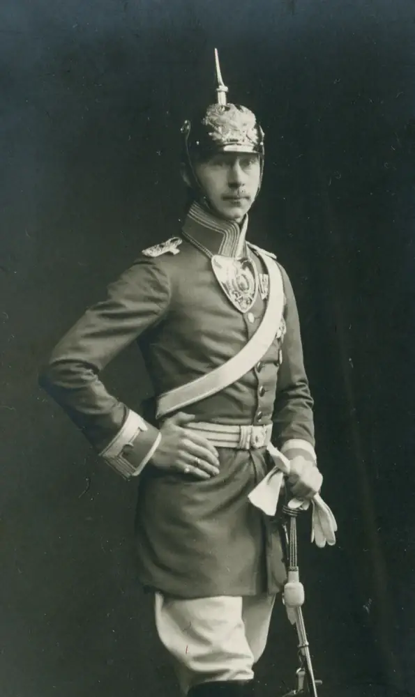 Kniestück: Kronprinz Wilhelm von Preußen mit Kürassierhelm, Ringkragen und Bandelier, die linke Hand in die Hüfte gestützt, die rechte am Degen, vor dunklem Grund