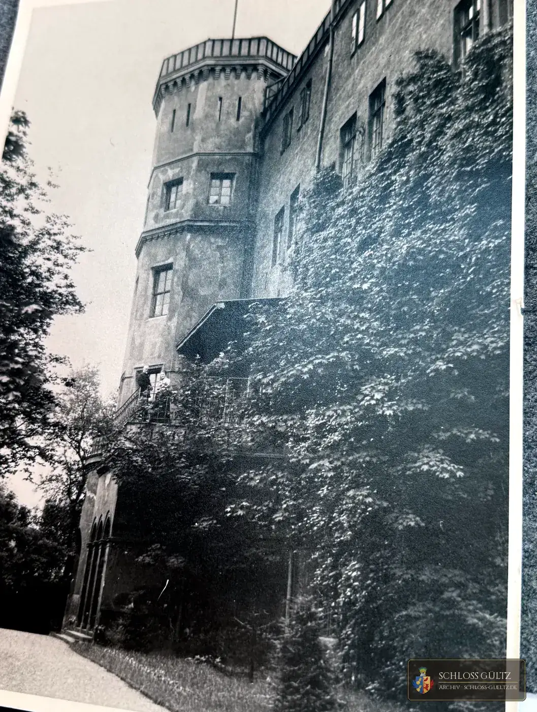 Efeubewachsener Schlossflügel mit achteckigem Turm, auf der Freitreppe zwei Personen